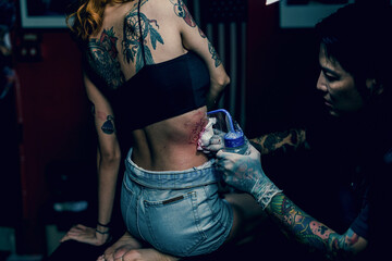 the tattoo artist wearing sterile white gloves while preparing cleaning the newly completed tattoo on a girl waist in a modern studio lowlight.
