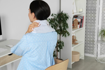 Woman using heating pad on neck at home