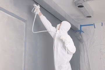 Decorator dyeing wall in grey color with spray paint indoors