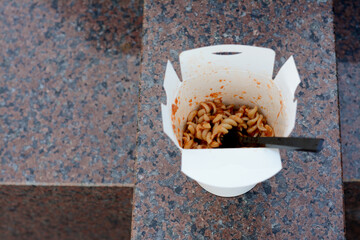 Paper box of takeaway noodles with fork on stone surface, above view and space for text. Street food