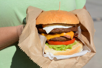 Woman holding delicious burger in paper wrap on blurred background, closeup