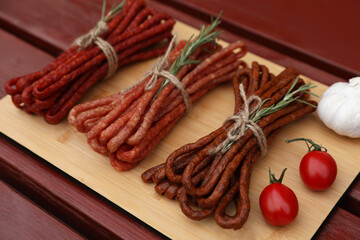 Bundles of delicious kabanosy with rosemary, tomatoes and garlic on wooden table