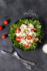Traditional caesar salad with chicken on a black plate on black table with napkin fork and knife.
