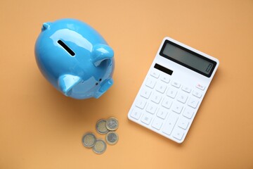 Piggy bank, coins and calculator on orange background, flat lay