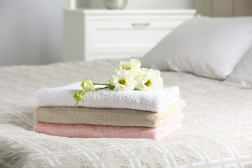 Fototapeta na wymiar Terry towels with beautiful flowers on bed indoors, space for text