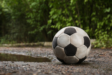 Fototapeta na wymiar Dirty soccer ball near puddle on ground, space for text