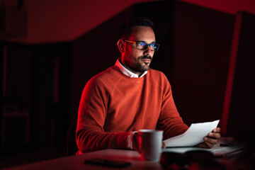 Serious-looking businessman, holding some papers, looking at the computer.