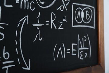 Fototapeta na wymiar Blackboard with different physical formulas written with chalk on white wall, closeup