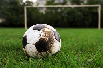 Dirty soccer ball on green grass outdoors, space for text