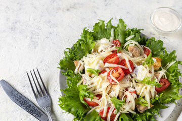 Traditional caesar salad with chicken on a plate on white table with napkin fork and knife.