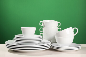 Set of clean dishware on white table against green background