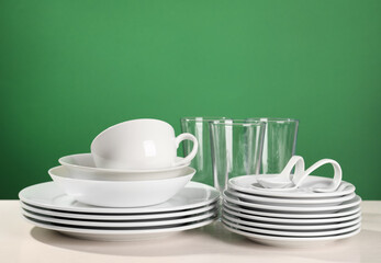 Set of clean dishware on white table against green background