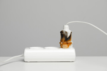 Inflamed plug in power strip on white table against grey wall. Electrical short circuit