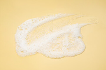 Smudge of white washing foam on yellow background, top view