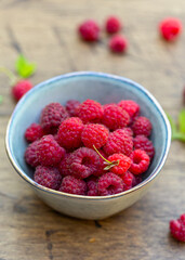 Bowl full of freshly gathered raspberries, close up, wooden background