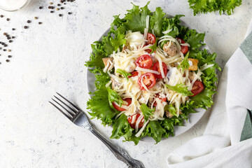 Traditional caesar salad with chicken on a plate on white table with napkin fork and knife.