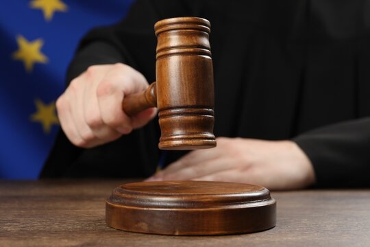 Judge with gavel at wooden table against flag of European Union, closeup