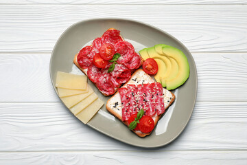 Tasty toasts with slices of sausages, tomatoes and cheese on white wooden table, flat lay