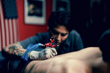 Professional tattooist makes the tattoo on a men waist, focusing on tattoo machines in a modern...