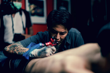 Professional tattooist makes the tattoo on a men waist, focusing on tattoo machines in a modern studio lowlight.