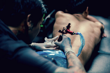 Professional tattooist makes the tattoo on a men waist, focusing on tattoo machines in a modern studio lowlight.