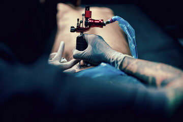 Professional tattooist makes the tattoo on a men waist, focusing on tattoo machines in a modern studio lowlight.