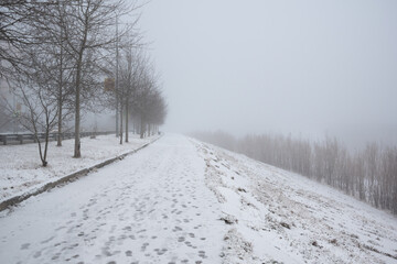 Frosty foggy morning in winter on the sidewalk and footprints in the snow.