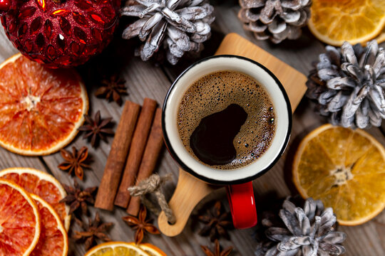 Christmas mood, holiday atmosphere. Red cup of coffee, pine cones, cinnamon, star anise and oranges. Top view on wooden table background.