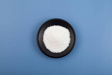 Sodium benzoate, sodium salt of benzoic acid in dark dish on blue. White crystalline powder,...