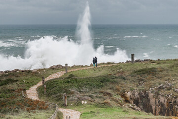 People watching the huge waves crashing on a breakwater. Weather alert on the coast with strong...