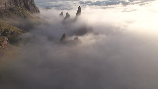 Panning view of Old Man of Storr rock formation at Isle of Skye, Scotland. Low flying clouds are beautifully covering the valley, mountain visible at background. Sunrise, wide view.