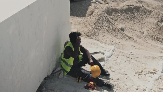 High angle of young adult African American forewoman having break taking off work gloves and hardhat, workday in quarry concept