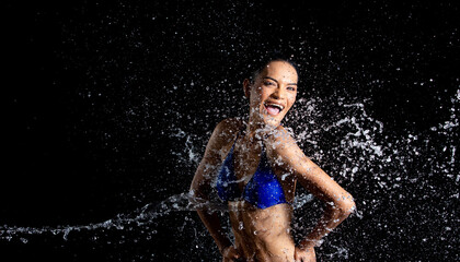 Tanned skin Asian woman in bikini poses in aqua studio. Splash Drops of water spread to body. Fun emotion female girl on water attack fluttering and stop motion freeze shot, black background isolated