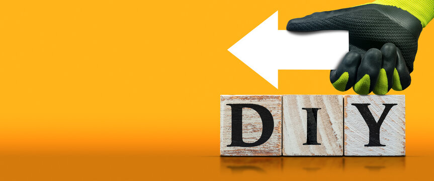 Text DIY (Do It Yourself), made of wooden blocks on orange and yellow background with copy space and a manual worker with protective work gloves holding an empty white directional sign (arrow shaped).