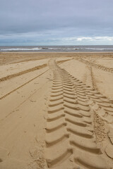tyre tracks on a sandy beach leading to the sea