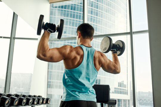 Man Doing Exercise With Dumbbell In The Gym. Photo Of A Sexy Muscular Man In Sportswear And Good Physique On Grey Background. Strength And Motivation, Sport, Fitness Goal