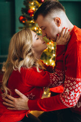 A charming couple in love in traditional Christmas red sweaters spend time near the Christmas tree