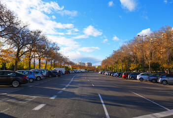 Parking lot cars. Empty road with cars on parking lot on street. Trees with yellow leaves against...