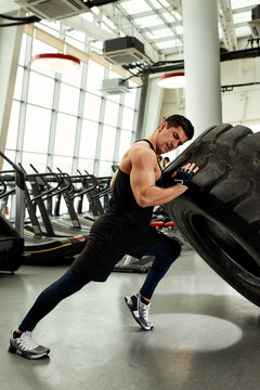 Muscular Fitness Man Moving Large Tire In Gym Center, Concept Lifting, Workout Training.