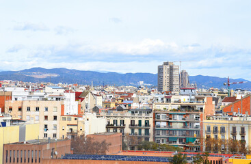 Fototapeta na wymiar Roofs of buildings. Barcelona Spain, high angle view city skyline. Mountains skyline. Rooftop view in Barcelona. Facade of old residential building at hills and mountain. Historic building in rock.