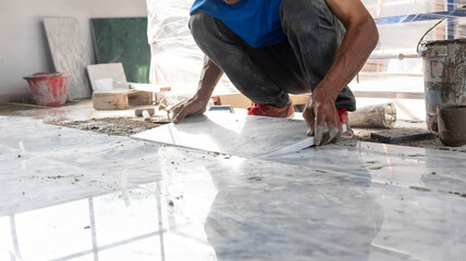 Tiler installing ceramic tiles on a floor.  construction workers laying tile over concrete floor using tile levelers, notched trowels and tile marble. 