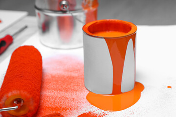 Cans of orange paint and roller on white table indoors
