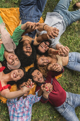 Obraz na płótnie Canvas Multiracial group of young people with raised arms and joined hands lying on the grass