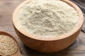 Quinoa flour in bowl and spoon with seeds on wooden table, closeup
