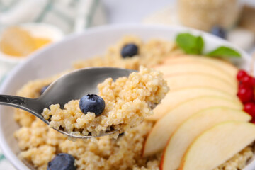 Spoon of delicious cooked quinoa with blueberry above bowl, closeup. Space for text