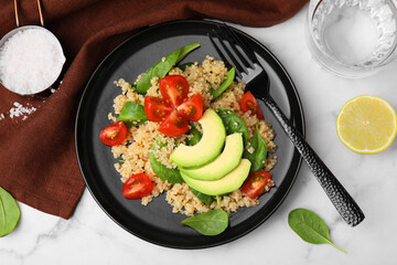 Delicious quinoa salad with tomatoes, avocado slices and spinach leaves served on white marble table, flat lay