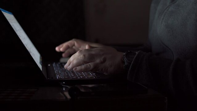 a man works at a laptop at night during a blackout. a programmer writes code. a hacker breaks into a network. emergency blackouts in the city due to the war. close-up of operator's hands behind laptop