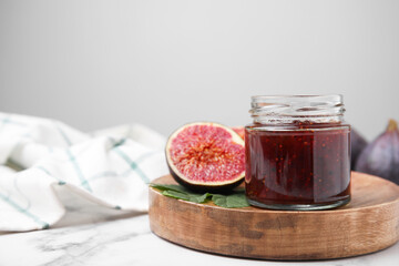 Glass jar of tasty sweet fig jam and fruits on white marble table. Space for text