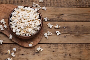 Bowl of tasty popcorn on wooden table, above view. Space for text