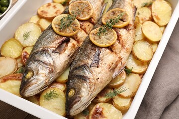 Baking tray with delicious baked sea bass fish and potatoes, closeup